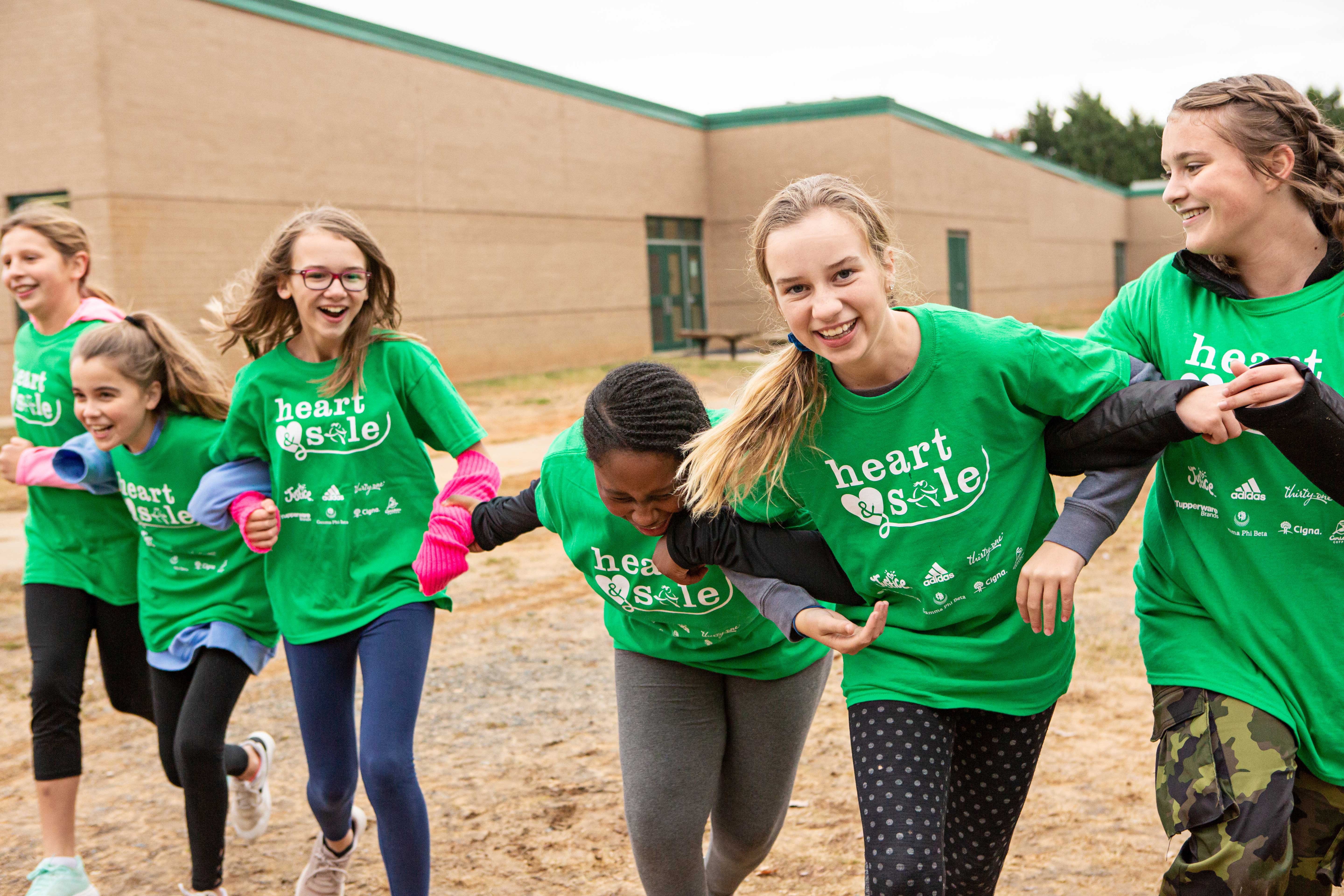 Two Girls on the Run participants smile at the camera while running at an outdoor practice in yellow shirts